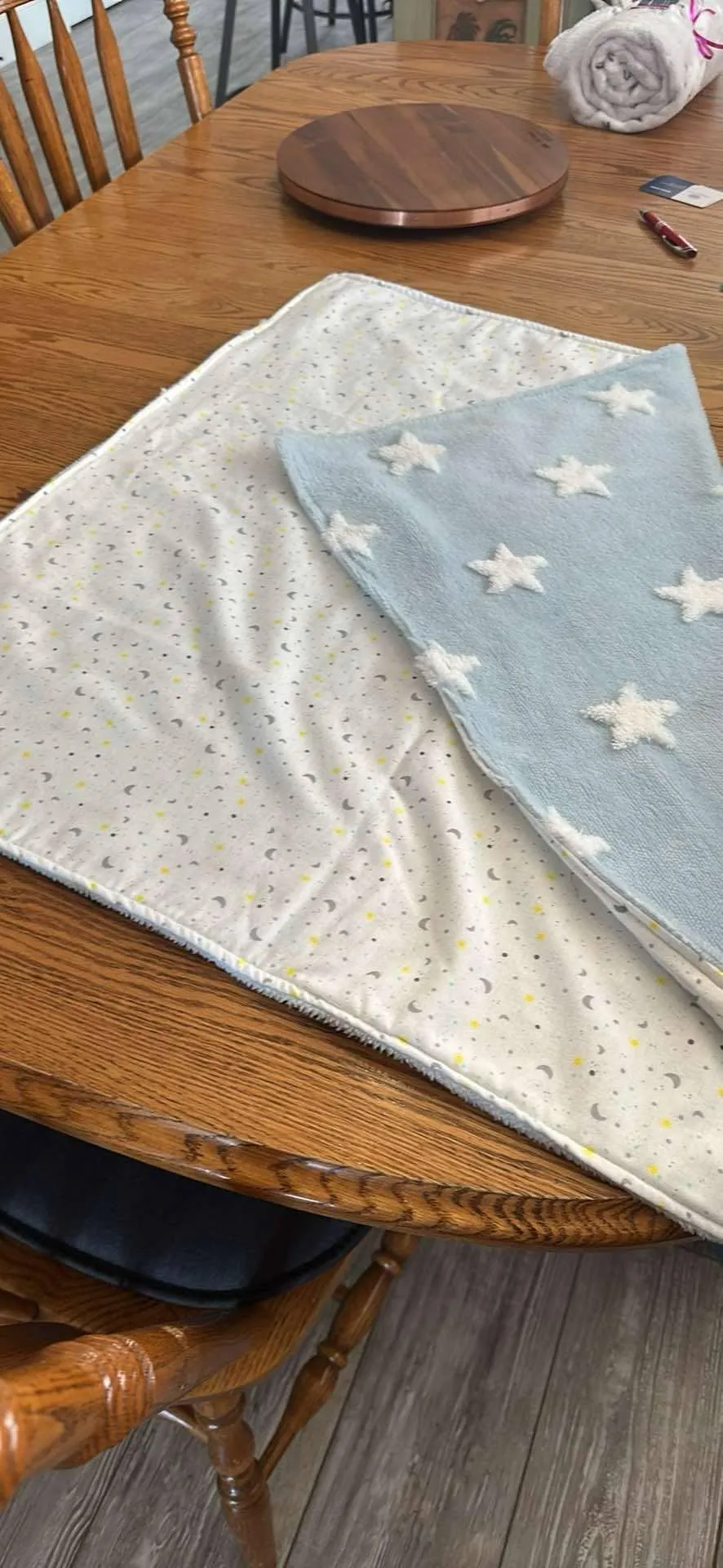 Two soft pastel baby blankets, one with moons and one with fluffy stars, laid on a wooden table