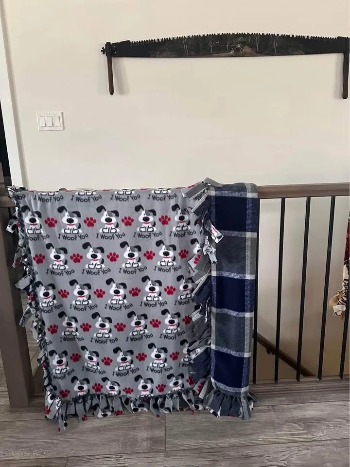 Grey I Woof You puppy print fleece tie blanket with a navy plaid blanket beside it on a railing